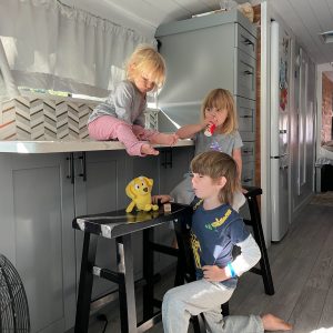 Three children in a skoolie small kitchen