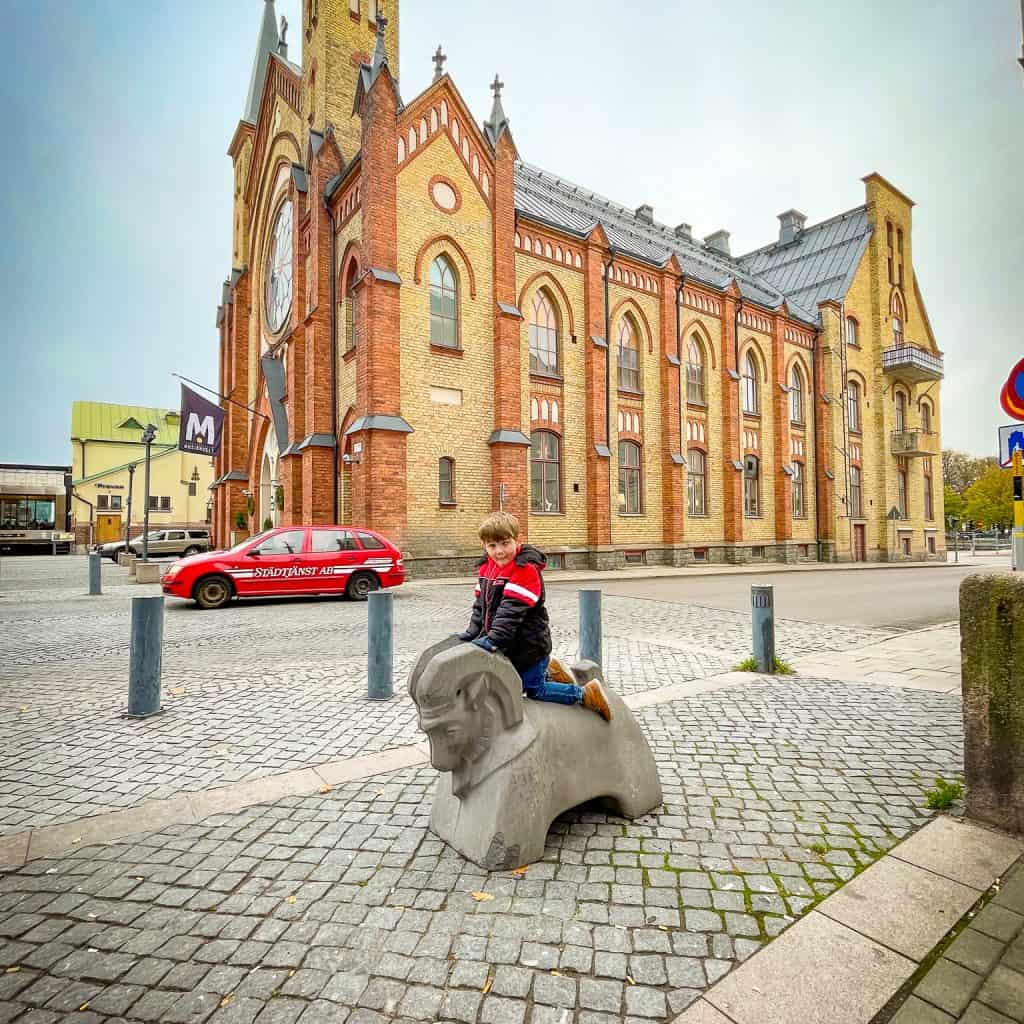 Landon sitting on a goat statue outside of a church in Gävle, Sweden | Destination Unknown