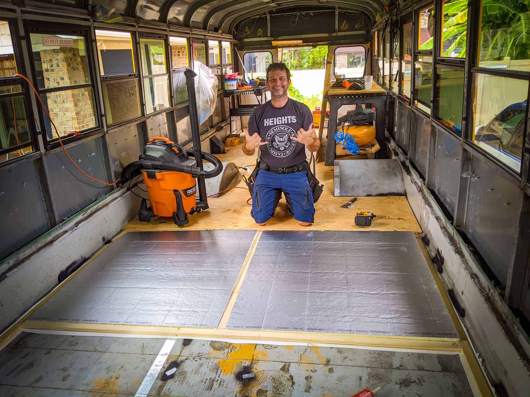 Man installing flooring furring strips and insulation. | what is a skoolie roof raise DESTINATION UNKNOWN