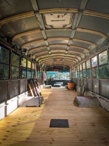 Empty school bus interior showing open walls with wood furring strips and subflooring. | what is a skoolie roof raise DESTINATION UNKNOWN
