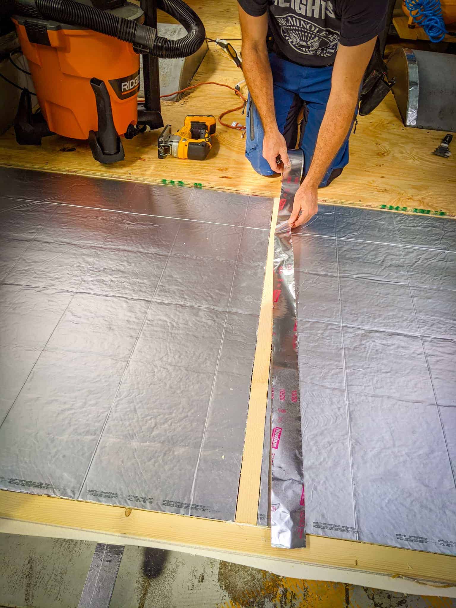 Man installing flooring furring strips and insulation. | what is a skoolie roof raise DESTINATION UNKNOWN