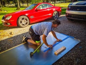 Man measuring sheet metal on the ground with ruler and marker | What is a skoolie roof raise? | Destination Unknown