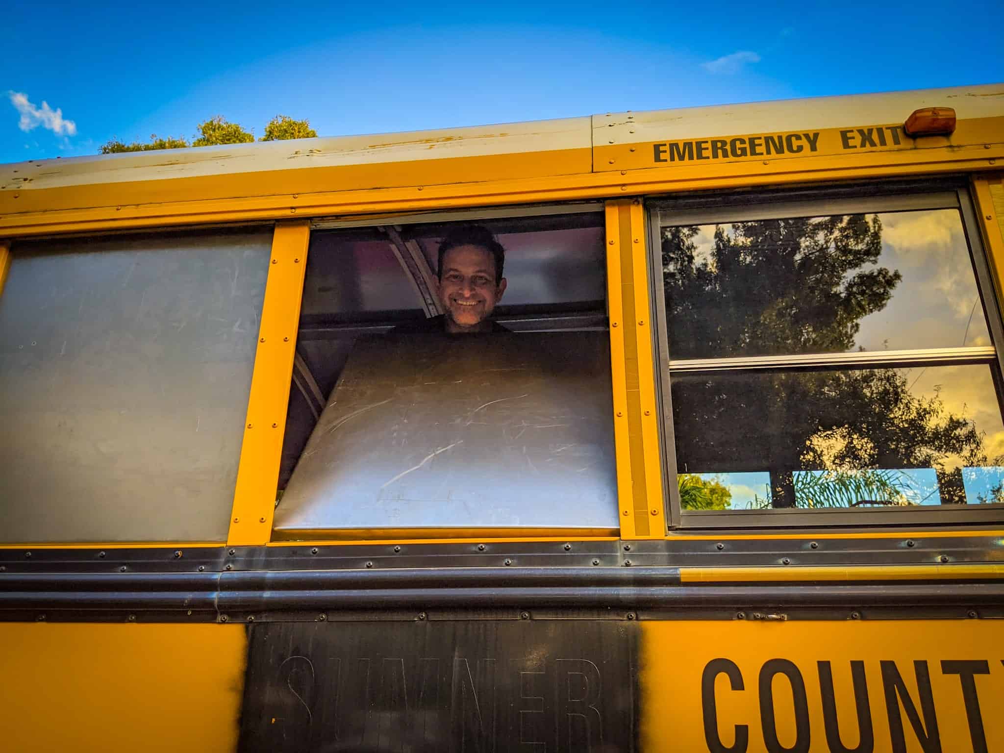 Man inserting a sheet metal frame into school bus window frame | what is a skoolie roof raise? | Destination Unknown