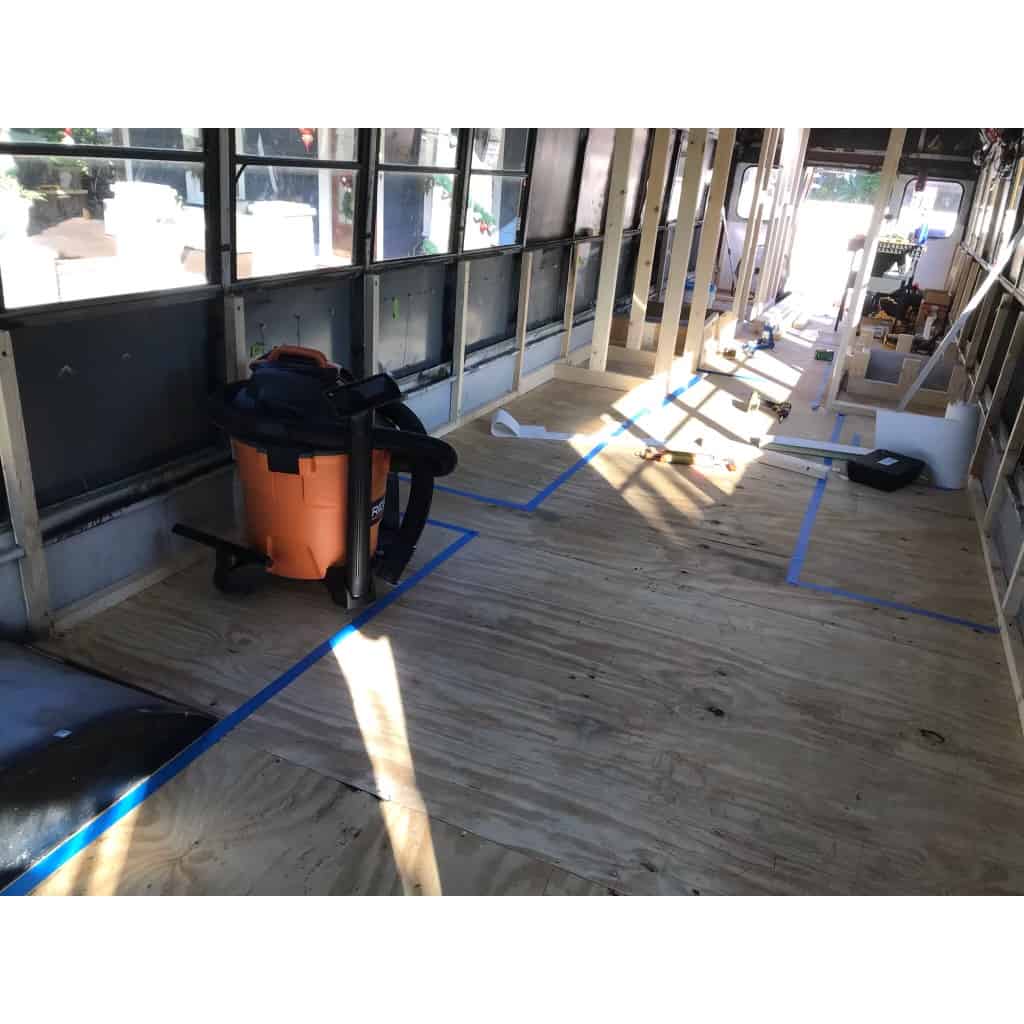 A skoolie build out at the framing stage. There is blue painters tape on the subfloor to show the location of items of the tiny home.