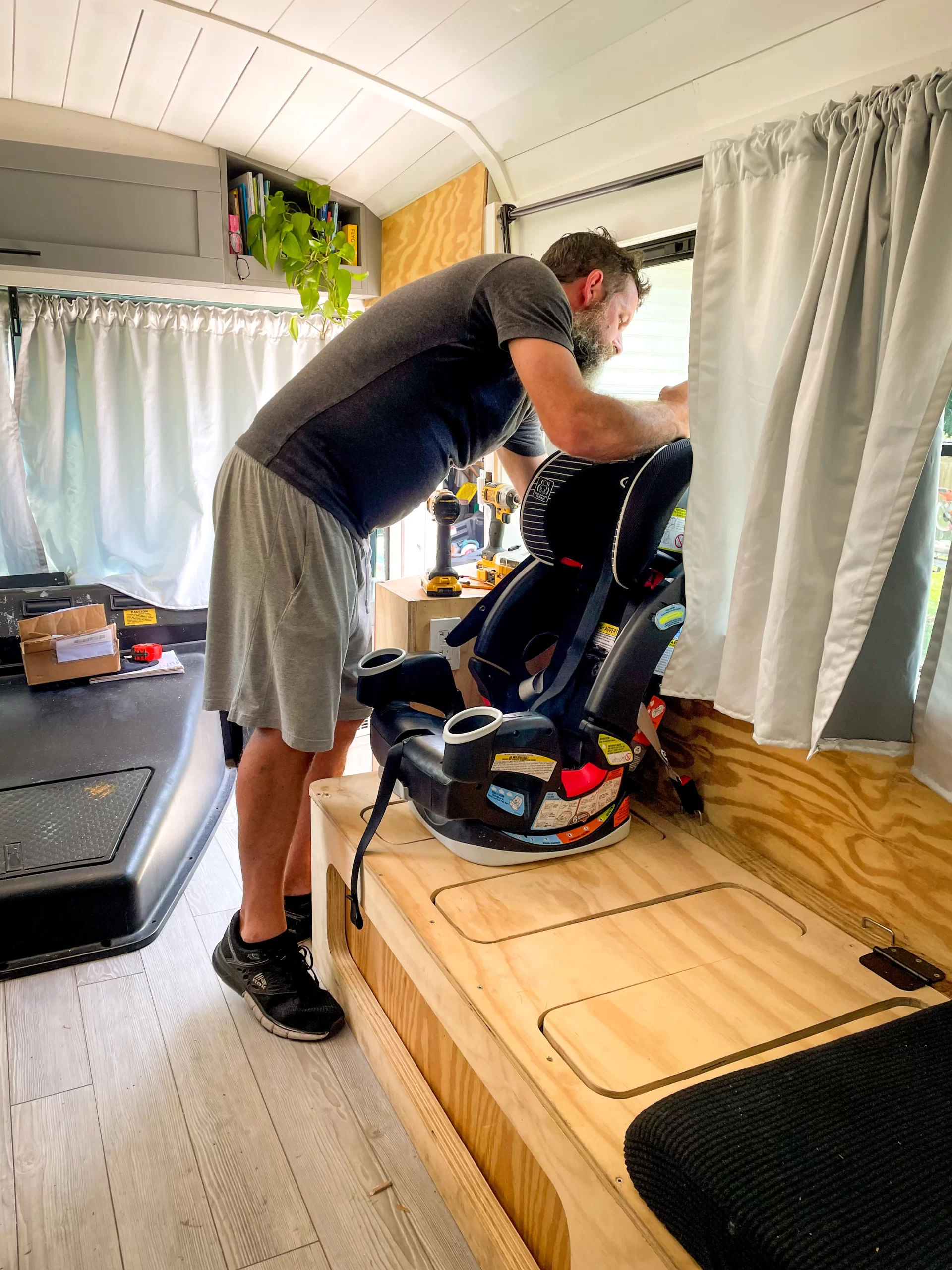 Man installing car seat to mounting brackets in school bus conversion.